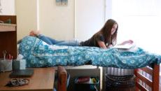 A student laying on a bed studying in a dorm room